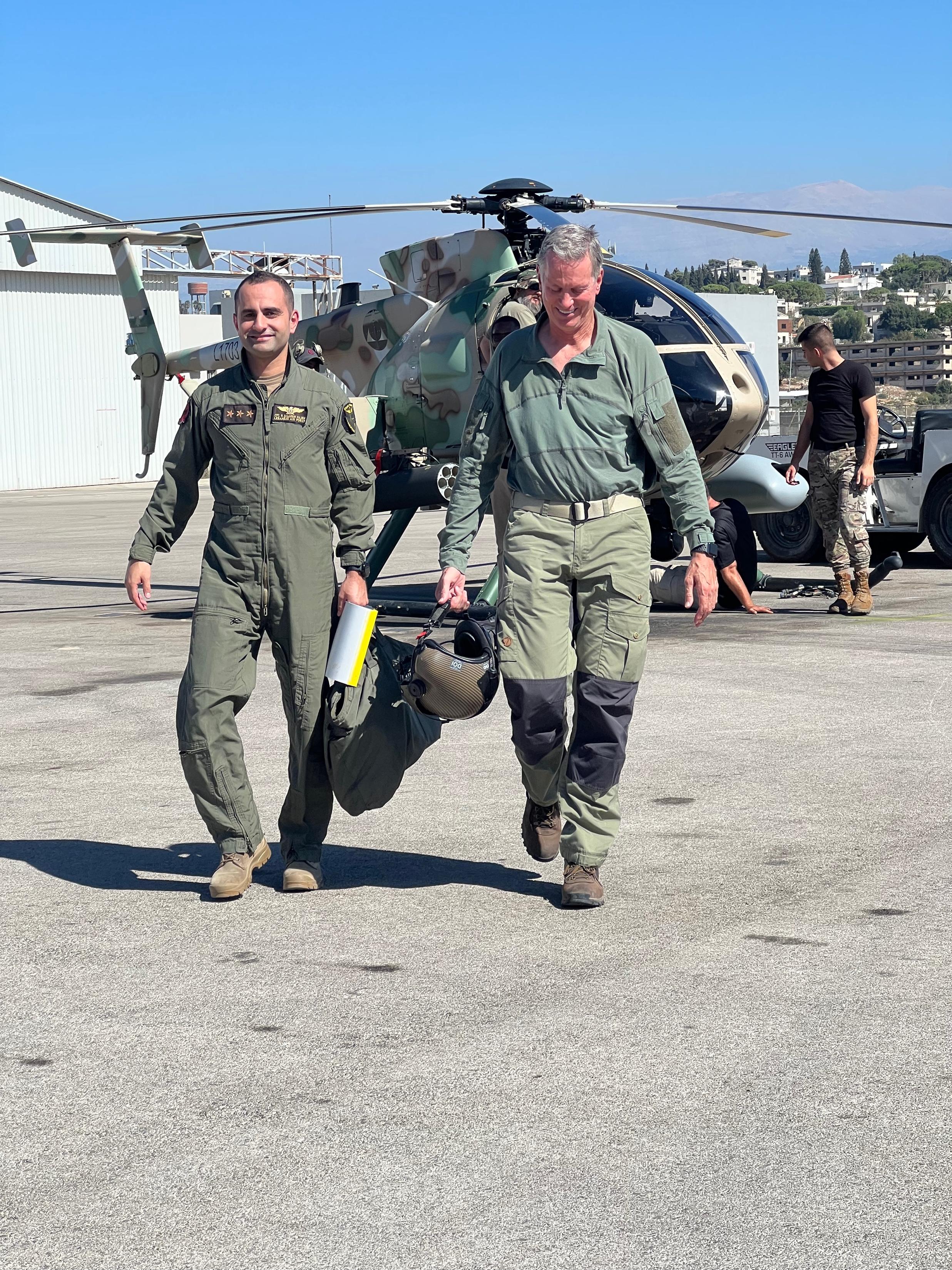 Instructor Thomas Perkins and a student walk away from a helicopter carrying their flight gear.